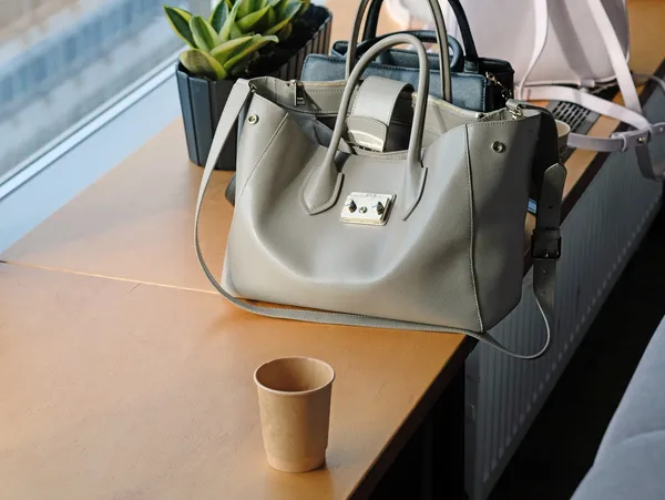 Gray leather handbag and empty paper cup